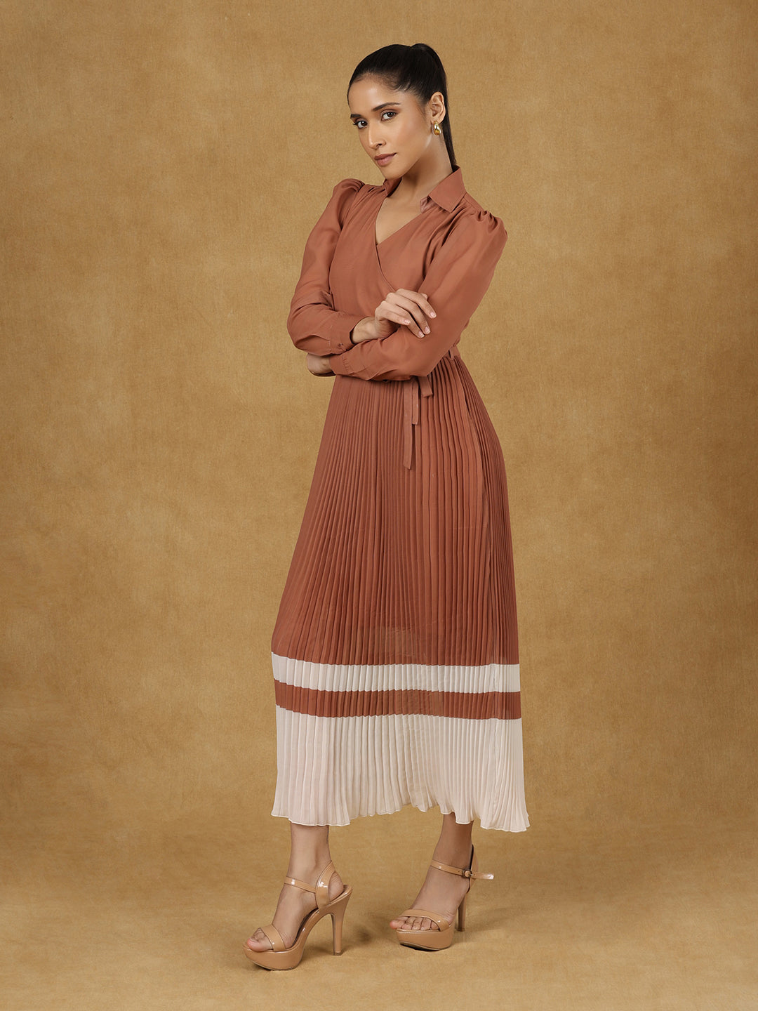 Brown wrap pleated dress displayed by model against beige background.