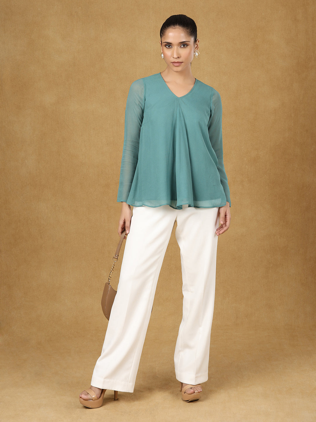 Green A-line top paired with white trousers and stylish heels.